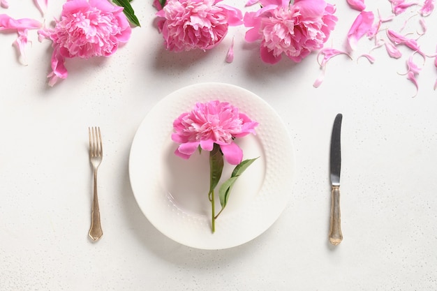 Festliche Tischdekoration mit rosa Pfingstrosenblüten auf einer weißen Tischansicht von oben