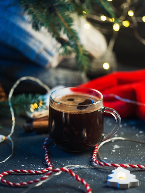 Festliche Weihnachtsdekoration, eine Tasse heißen Espresso-Kaffee auf dem Tisch mit Weihnachtsbaumzweigen, Santas rote Mütze, Strickkleidung