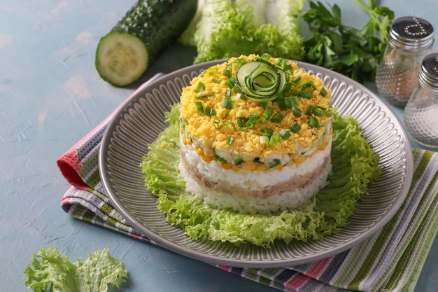 Festlicher Blätterteigsalat mit Kabeljauleber, Reis, Mais und Gurke auf einem Teller auf hellblauem Hintergrund