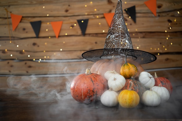 Festlicher Halloween-Hintergrund. Unter dem Hexenhut liegen orangefarbene und grüne Kürbisse mit dichtem Rauch um sie herum.
