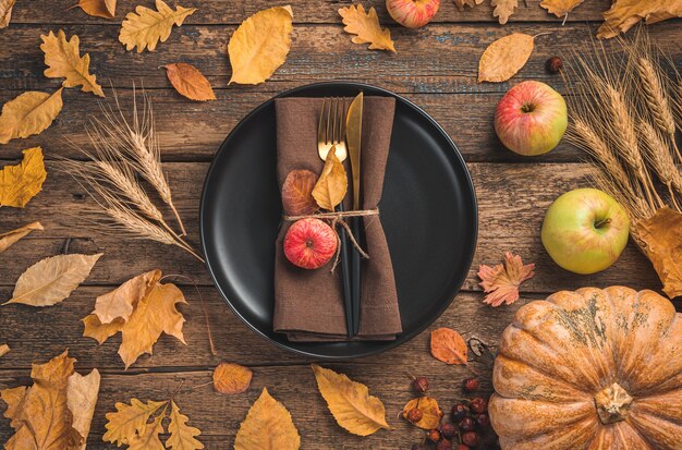 Festlicher Herbsthintergrund mit einem Tellerserviettenbesteck Kürbis und Herbstlaub