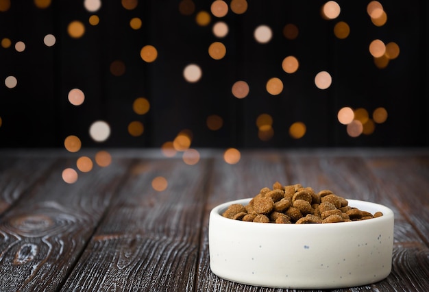 Festlicher Hintergrund mit Tierfutter Futterkörner liegen in einem Teller auf einem Holztisch mit Weihnachtsbeleuchtung