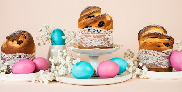 Festlicher Osterkuchen mit Rosinen und bunten Eiern, verziert mit weißen Frühlingsblumen. Horizontales Foto, Pastellhintergrund