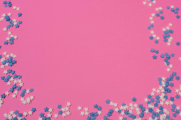 Festlicher Rahmen aus bunten Pastellstreuseln auf rosafarbenem Hintergrund Kopierfläche oben Streuen Sie Zucker mit Kugeln und Sternendekoration für Kuchen und Backwaren Draufsicht oder flache Lage