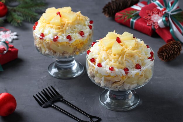 Festlicher Salat mit Hühnchen, Ananas, Käse und Eiern in portionierten Schalen auf dunkelgrauem Hintergrund. Silvester-Stillleben.