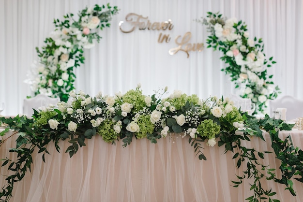 Festlicher Tischbogen, dekoriert mit einer Komposition aus weißen, rosafarbenen Blumen und Grün im Bankettsaal Tisch Jungvermählten bedeckten eine Tischdecke im Bankettbereich bei der Hochzeitsfeier