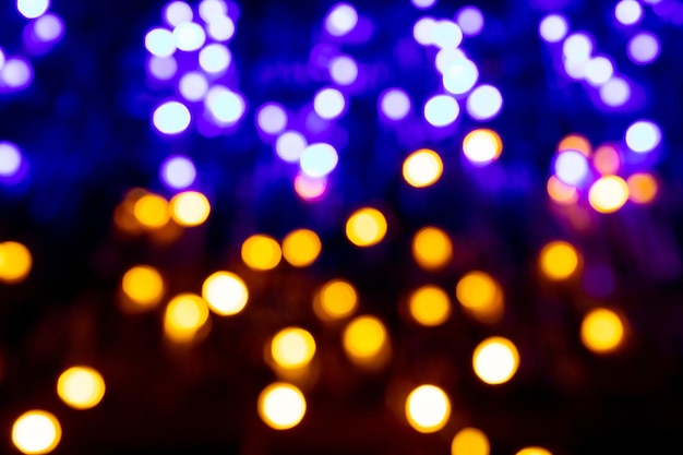 Festlicher Weihnachts- und Neujahrshintergrund mit verschwommenen gelben und blauen Bokeh-Lichtern auf schwarzem Hintergrund