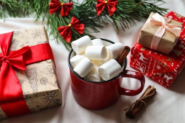 Festlicher Weihnachtshintergrund mit Weihnachtsbaum, rote Tasse mit Marshmallows, Geschenken, Zimtstangen