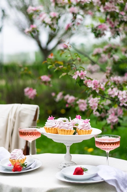 Festliches Frühlingsgedeck mit romantischer Tischdekoration und Dessert im Blütengarten vertikal