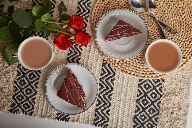 Festliches Frühstück mit Kirschschokoladenkuchenstücken, Kaffeetassen, roten Rosen und ästhetischer Flachlage zum Valentinstag