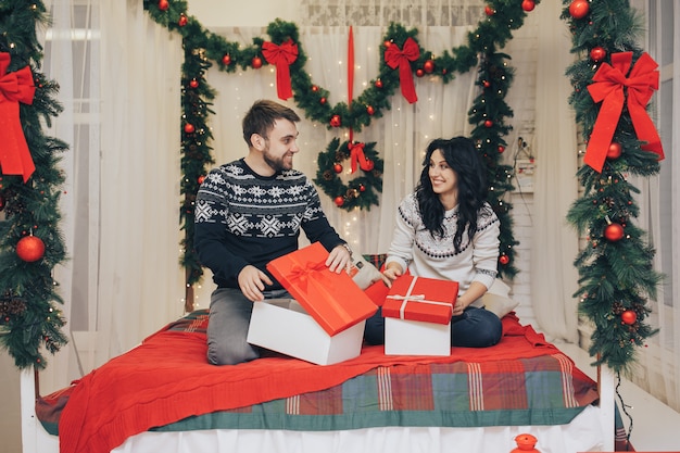 Festliches junges Paar, das Geschenke auf Weihnachtshintergrund austauscht