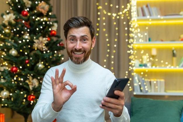 Festliches Online-Shopping Ein junger Mann hält ein Telefon in den Händen, kauft online ein und kauft Geschenke