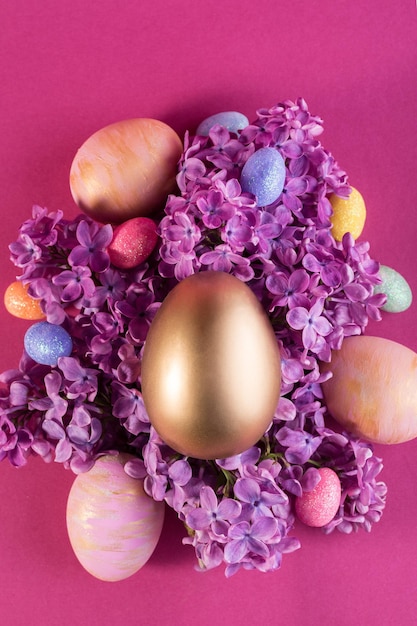 Festliches Osterkonzept mit großem dekorativem Goldei auf fliederfarbenen Blüten vor kräftig rosafarbenem Hintergrund Festliche Frühlingskulisse