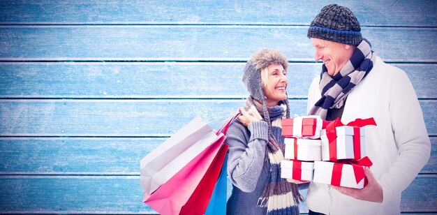 Festliches reifes Paar, das Weihnachtsgeschenke gegen Holzbohlen hält