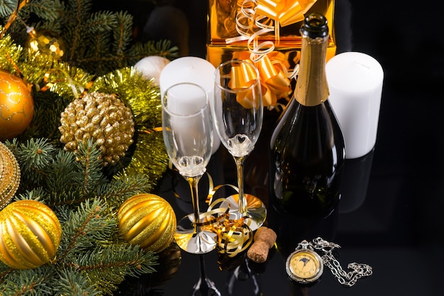 Festliches Stilleben mit hohem Winkel - Nahaufnahme von eleganten Champagnergläsern auf schwarzem Hintergrund mit Taschenuhr, weißen Kerzen, goldenen Geschenken und immergrünem Dekor mit Weihnachtskugeln und Lametta