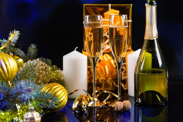 Festliches Stillleben - Zwei Gläser Sekt mit Flasche, Kerzen, Geschenken und Weihnachtsschmuck auf schwarzem Hintergrund