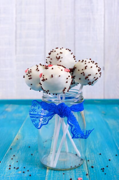 Festtagsleckereien. Cake Pops. Kekskuchen in der weißen Schokoladenglasur auf einem hellen blauen hölzernen Hintergrund. Vertikale Ansicht.