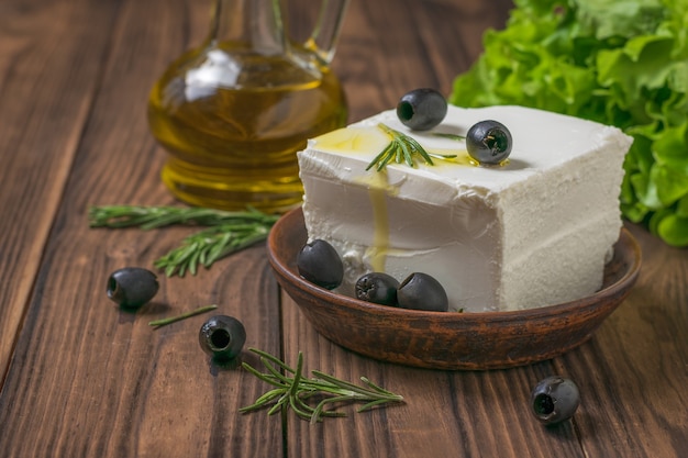 Feta-Käse mit Oliven, Olivenöl und Salat auf einem Holztisch. Salat mit Käse und Gemüse.