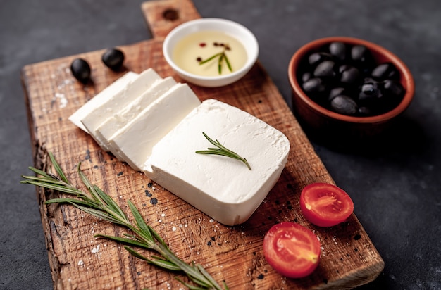 Feta-Käse, mit Rosmarin, Tomaten, Oliven auf einem Steinhintergrund.