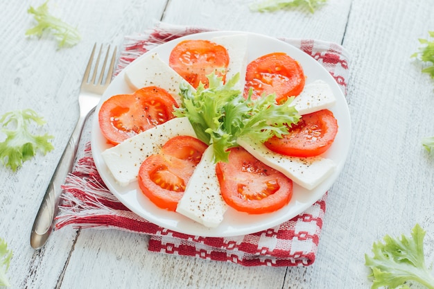 Feta-Käsescheiben mit Tomate auf weißem Teller.