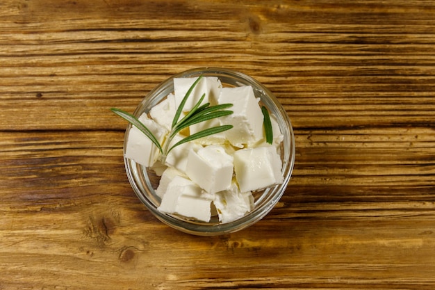 Feta-Käsewürfel mit Rosmarin in Glasschüssel auf einem Holztisch Draufsicht