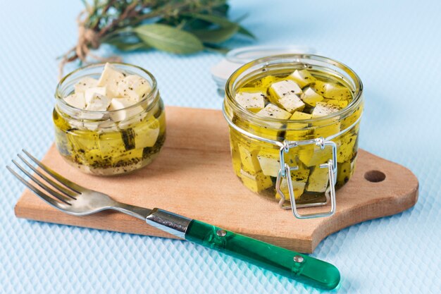 Feta marinado en un frasco de vidrio y especias sobre fondo azul