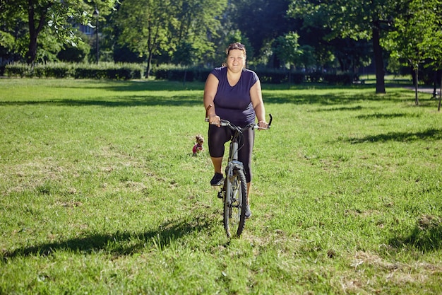 Fette Frau fährt Fahrrad im Parkkonzept der Körperpositivität und des gesunden Lebensstils