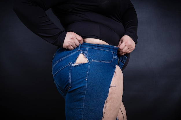 Fette Frau in zerrissenen Jeans auf schwarzem Hintergrund Foto in hoher Qualität