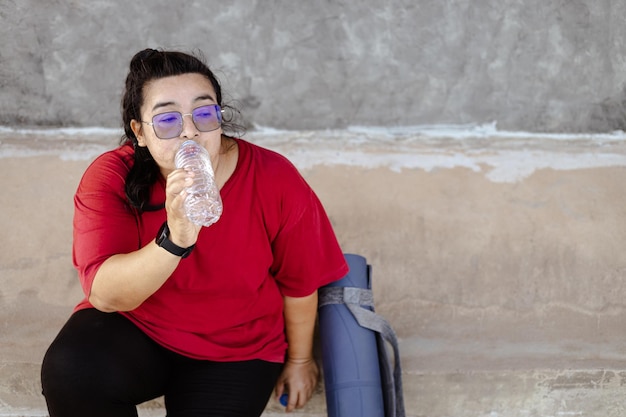 Fette Frau trainiert und macht eine Pause, um Wasser zu trinken