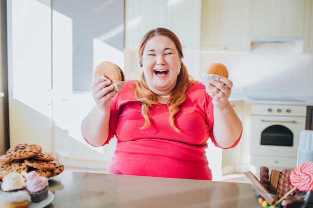 Fette junge Frau in der Küche, die Junk Food sitzt und isst.