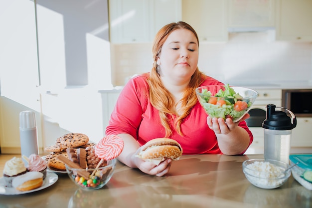 Fette junge Frau in der Küche, die sitzt und Essen isst