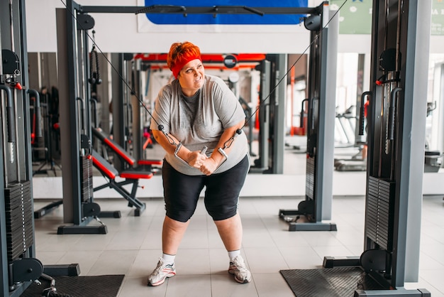 Fette verschwitzte Frau, die Übungsmaschine im Fitnessstudio verwendet. Kalorien brennende, fettleibige weibliche Person im Sportverein