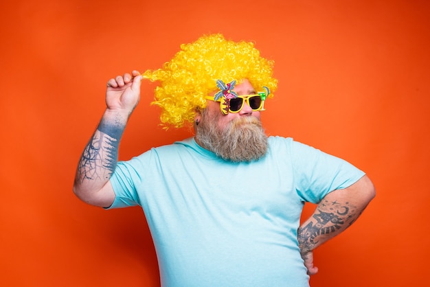 Fetter glücklicher Mann mit Barttattoos und Sonnenbrille hat Spaß mit der gelben Perücke