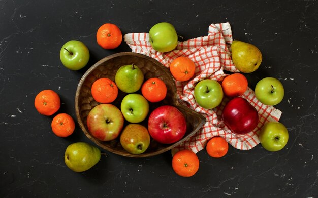 Fettes Laienfoto - bunte Früchte - Äpfel, Birnen und Mandarinen auf schwarzem Marmor wie Brett.