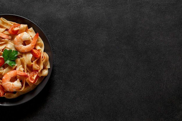 Fettuccine gekocht mit Garnelen- und Tomatensoße in der grauen Platte auf Draufsichtraum des dunklen Hintergrundes, um Text zu kopieren