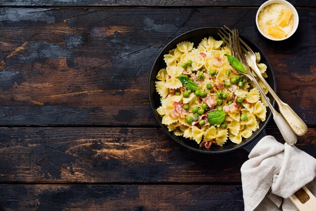 Fettuccine-Nudeln mit Speck und grünen Erbsen und Parmesan in alter Pfanne auf alter dunkler Holzoberfläche