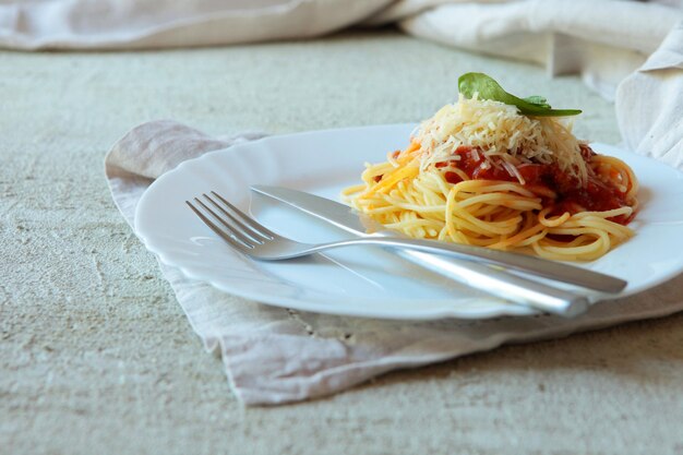 Fettuccine de pasta a la boloñesa con salsa de tomate en un plato blanco. Carlic y sal y tomates sobre un fondo de hormigón con servilletas de lino.