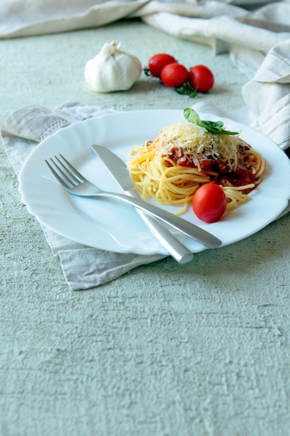 Fettuccine de pasta a la boloñesa con salsa de tomate en un plato blanco. Carlic, sal y tomates sobre hormigón