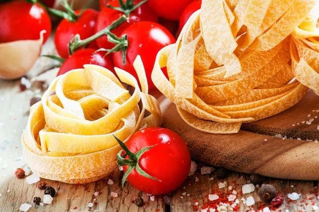 Fettuccine de pasta italiana seca en forma de nidos tomates cherry perejil eneldo ajo aceite de oliva en una jarra sal y especias en el antiguo fondo de madera enfoque selectivo