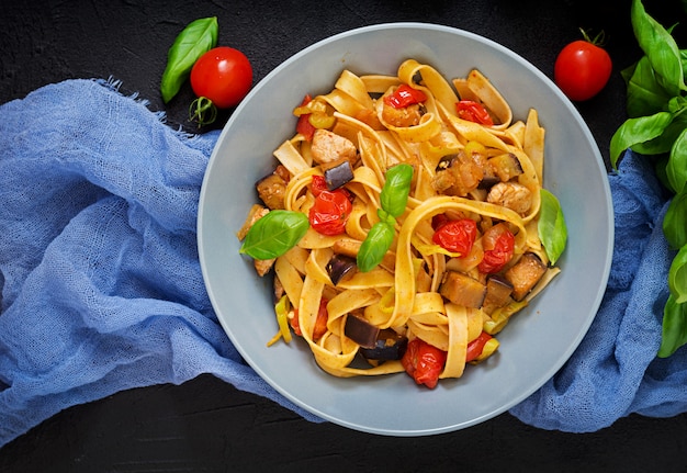 Fettuccine de pasta con tomate, berenjena y filete de pollo en un tazón. Endecha plana.