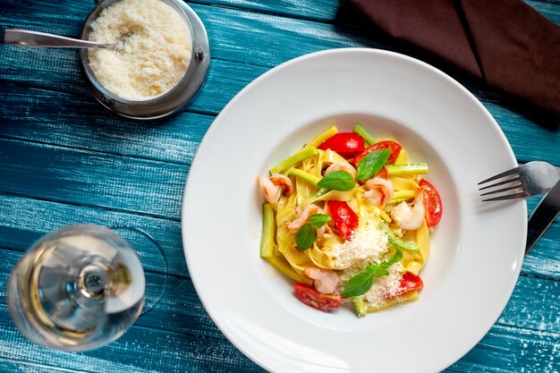 Fettuccini-Nudeln mit Garnelen, Tomaten, Avocado und geriebenem Parmesan auf hölzerner blauer Oberfläche