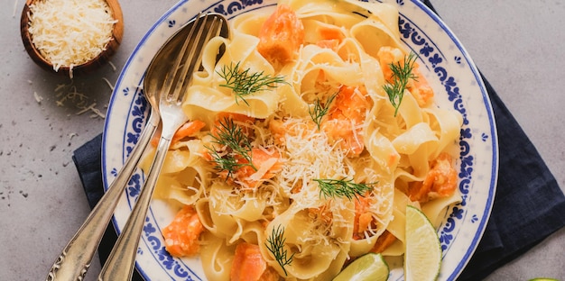 Fettucine-Nudeln mit Lachs und Parmesankäse in cremiger Soße in Keramikplatte auf altem grauem Betonhintergrund. Ansicht von oben.