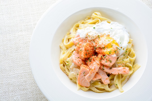 Fettucine con salmón, huevo y queso parmesano, servido en plato blanco.