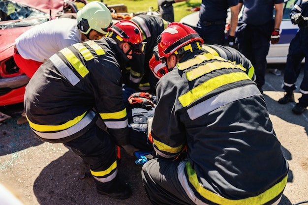 Feuerwehrleute kümmern sich um andere Feuerwehrleute und ziehen ihn aus einem verunglückten Auto.