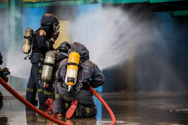 Feuerwehrmänner, die Wasser vom Schlauch für Feuerbekämpfung am Feuerwehrentraining der Versicherungsgruppe verwenden