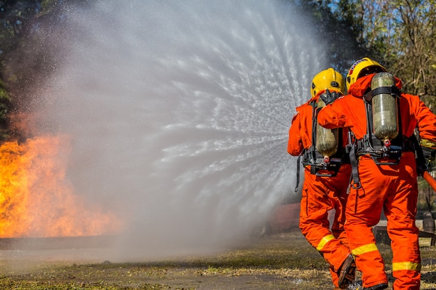 Feuerwehrmann, der Feuerlöscher und Wasser vom Schlauch für Feuerbekämpfung verwendet