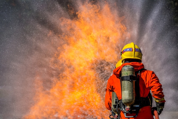 Feuerwehrmann, der Feuerlöscher und Wasser vom Schlauch für Feuerbekämpfung verwendet