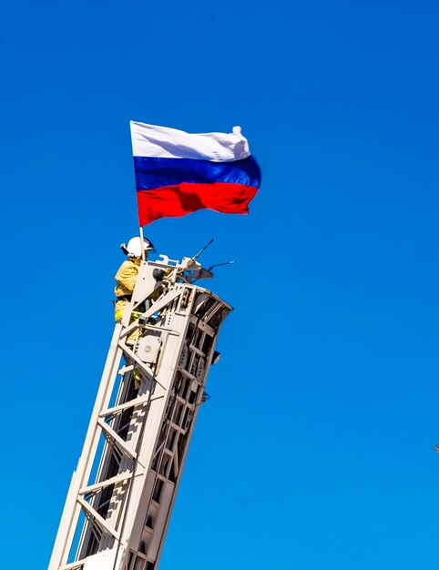 Feuerwehrmann sichert eine russische Flagge auf Feuerleiter auf blauem Himmel