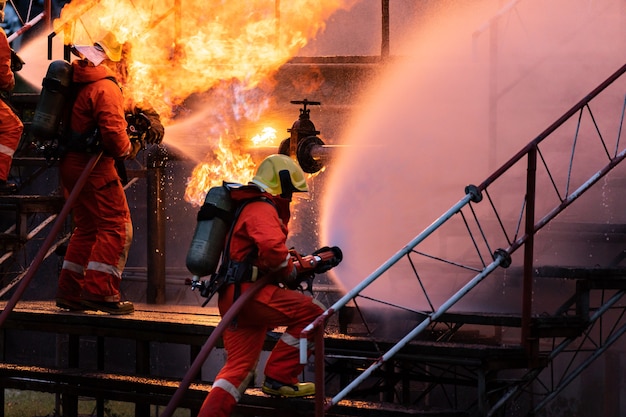 Feuerwehrmann-Team, das Feuerlöscher vom Typ Wassernebel verwendet, um mit der Flamme von Ölpipeline-Leck und Explosion auf Bohrinsel und Erdgastank zu kämpfen. Feuerwehrmann- und Arbeitsschutzkonzept.