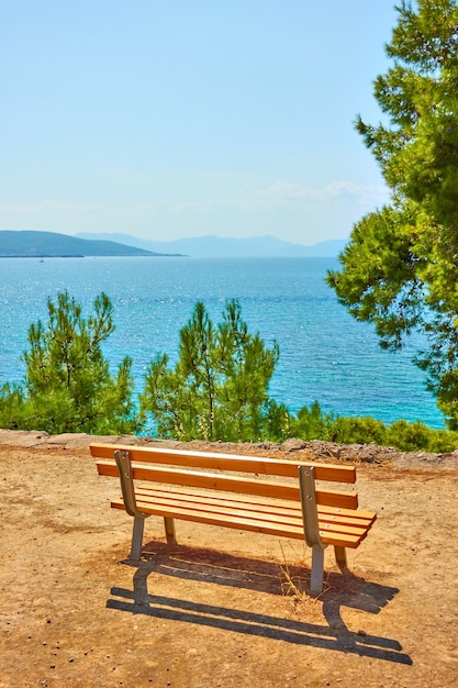 Öffentlicher Park mit Bank an der Küste des Meeres in der Stadt Ägina an einem sonnigen Sommertag, Insel Ägina, Griechenland - Landschaft